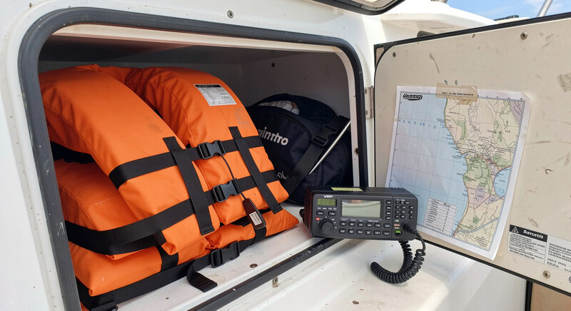 Orange life jackets stacked in a boat locker beside a VHF radio and a chart, ready for a day on the bay.