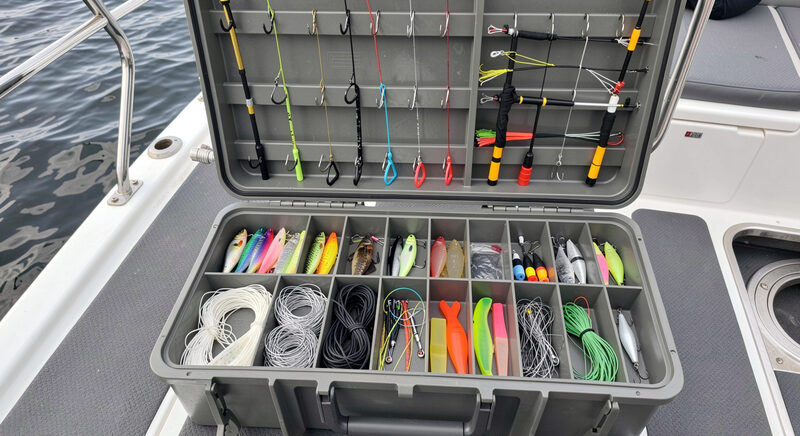 A tackle tray open on a boat deck showing umbrella rigs, wire line jigs and soft plastics laid out in neat rows.